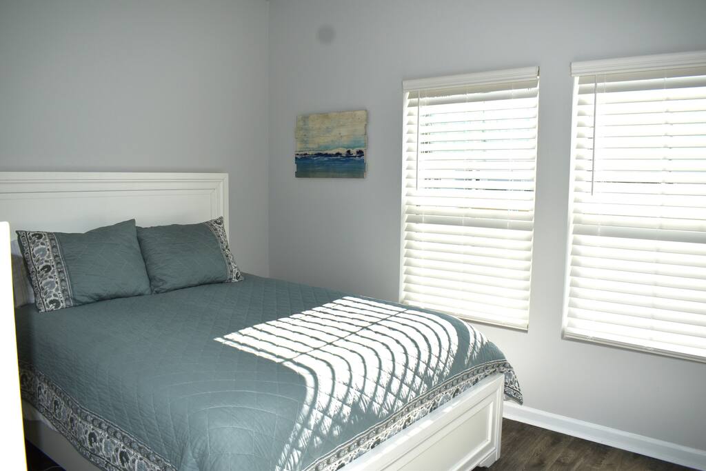 Cozy and bright guest bedroom with a queen-size bed, fresh linens, and a modern coastal vibe. Large windows bring in natural light, and a tall dresser offers ample storage. Perfect for restful nights after exploring the area!