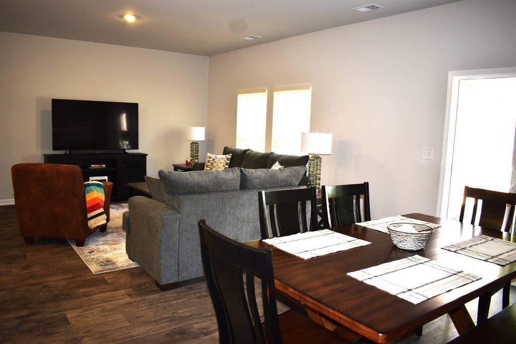 Open-concept living and dining area with a large sectional, smart TV, and spacious dining table — ideal for gathering, relaxing, and enjoying meals together in comfort.