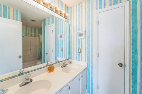 Relax and refresh in your spacious private bathroom, featuring a double vanity with ample counter space and a shower/tub combination for your convenience. The bright, striped wallpaper adds a cheerful coastal vibe to your stay.