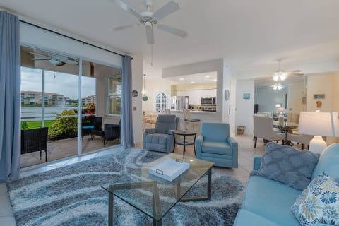 A bright, modern living room with comfortable seating, a plush area rug, and a glass coffee table. Large glass doors open to a screened lanai, creating a seamless indoor-outdoor feel.
