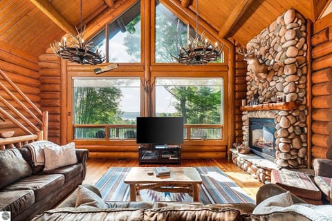 Cozy up in the stunning great room with soaring ceilings, a grand stone fireplace, and massive windows offering peaceful views of the trees and lake. A true rustic-luxury experience perfect for relaxing.