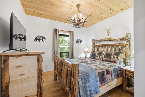 Cozy rustic bedroom with log furnishings, wood ceiling, and peaceful nature views