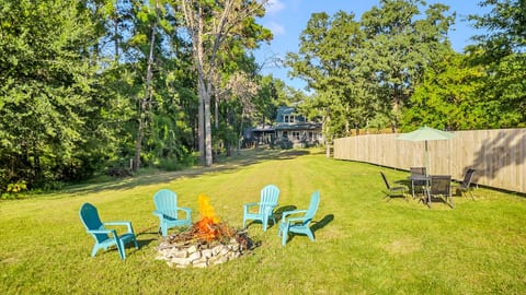 This stunning lakeside retreat offers maximum relaxation with a firepit ringed by Adirondack chairs on a grassy lawn. The view overlooks a calm lake with boat docks and jetties under a clear sky, promising a peaceful outdoor escape.