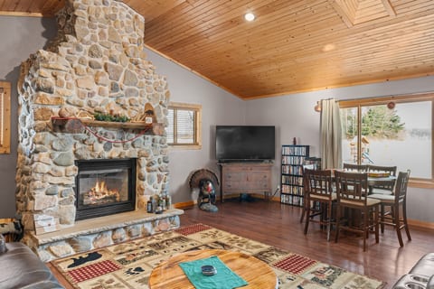 Cozy great room with stone fireplace, vaulted wood ceiling, and bright dining area
