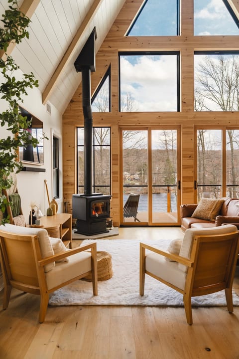 This bright, open-concept living space features soaring vaulted ceilings, floor-to-ceiling windows with panoramic lake views, and a cozy wood-burning stove perfect for chilly evenings. Relax, connect, and take in the view.
