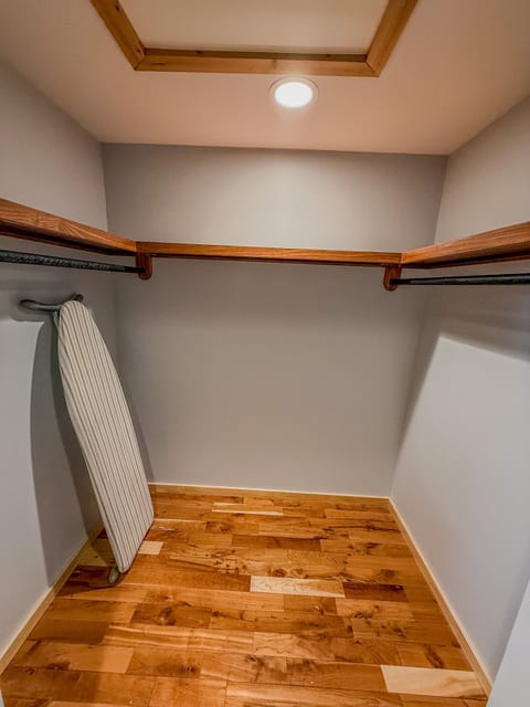 Bright walk-in closet with hardwood floors, dual rods, and ironing board