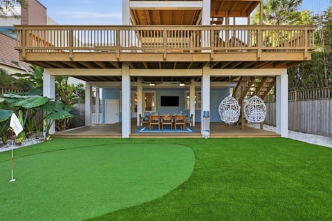This private outdoor oasis features a custom putting green, shaded dining area with TV, and cozy hanging lounge chairs — perfect for relaxing after a beach day.