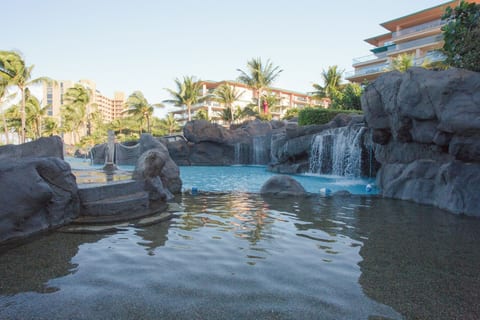 Kids shallow pool area with waterfall and waterslide in the background.