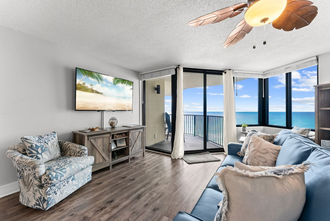 Beautiful beachfront living space featuring a large flat-screen TV and floor-to-ceiling windows overlooking the emerald coast.