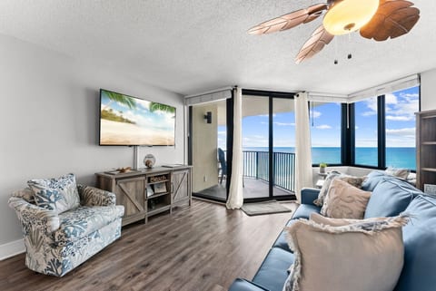 Beautiful beachfront living space featuring a large flat-screen TV and floor-to-ceiling windows overlooking the emerald coast.