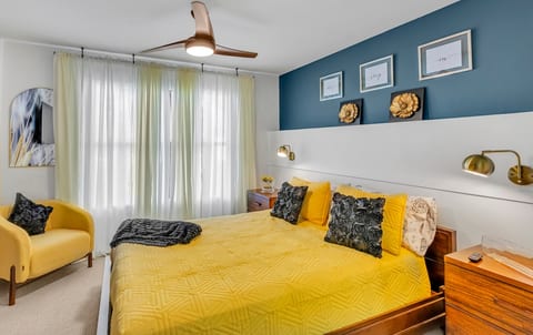 Sunny primary bedroom with queen bed and soft, hotel-style bedding.