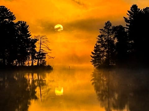 Golden light floods the sky as the sun rises over the still lake, reflecting perfectly in the water between tall pines. Mornings here feel magical, serene, and completely private.