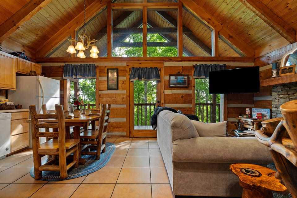 Big windows fill the open living and dining area at Nestled Oaks with natural light and peaceful forest views.