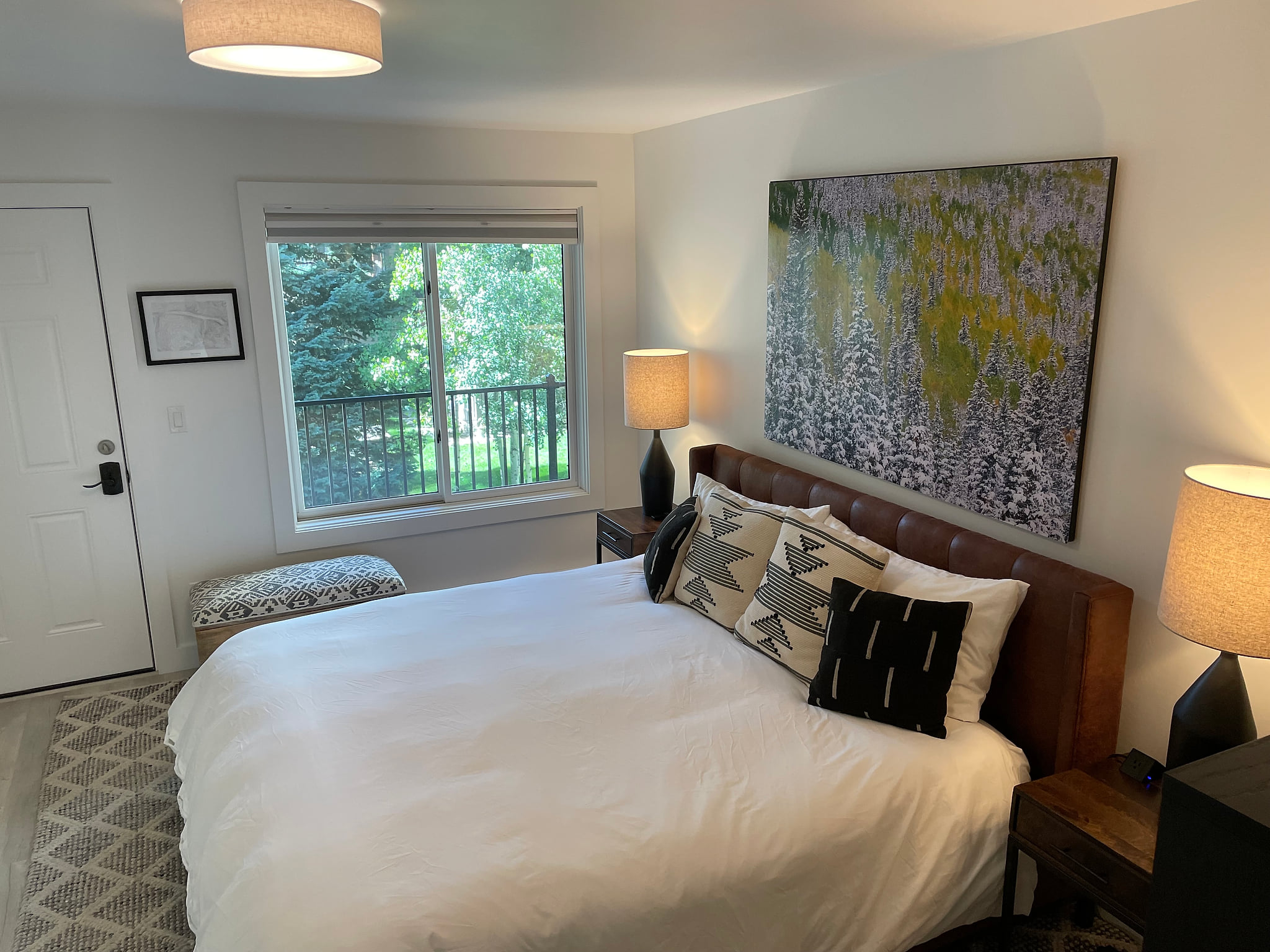 Bright, cozy bedroom with large bed, stylish decor, and leafy window views.