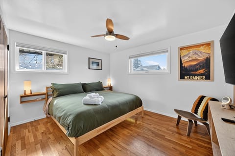 Bright king bedroom with hardwood floors, ceiling fan, and smart TV