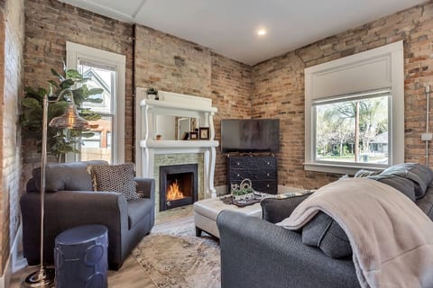Bright, stylish living space with exposed brick walls, modern décor, and cozy fireplace. Enjoy natural light, smart TV, comfortable seating, and a welcoming layout—perfect for relaxing after exploring the city or working remotely.