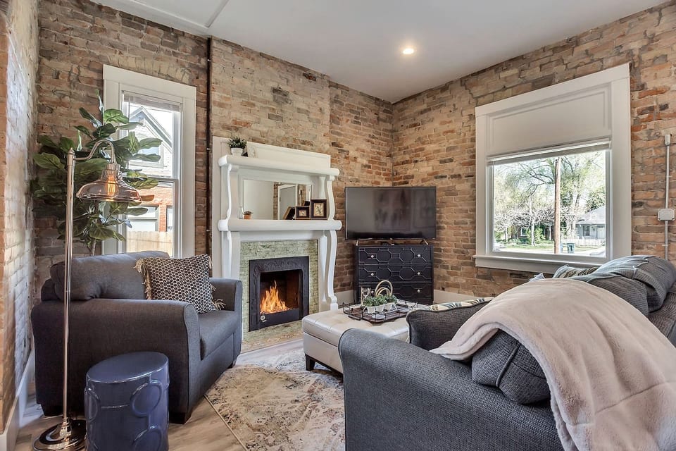 Bright, stylish living space with exposed brick walls, modern décor, and cozy fireplace. Enjoy natural light, smart TV, comfortable seating, and a welcoming layout—perfect for relaxing after exploring the city or working remotely.