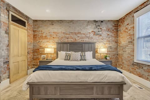 Spacious, stylish bedroom with exposed brick walls, plush king bed, premium linens, and soft lighting. Enjoy a smart TV, ample storage, and a calm, cozy atmosphere—perfect for restful nights in a modern loft-style retreat.