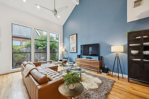 Unwind in this sun-drenched living room featuring a dramatic vaulted ceiling, smart TV, leather couch, and curated mid-century modern touches.