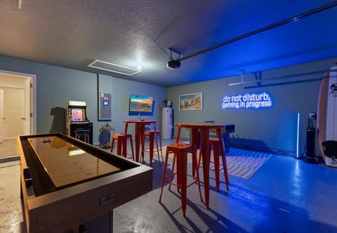 Neon-lit game garage with shuffleboard, arcade, bar tables and TV lounge.