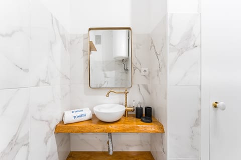 Sleek bath with marble tiles, vessel sink, brass fixtures & wood vanity