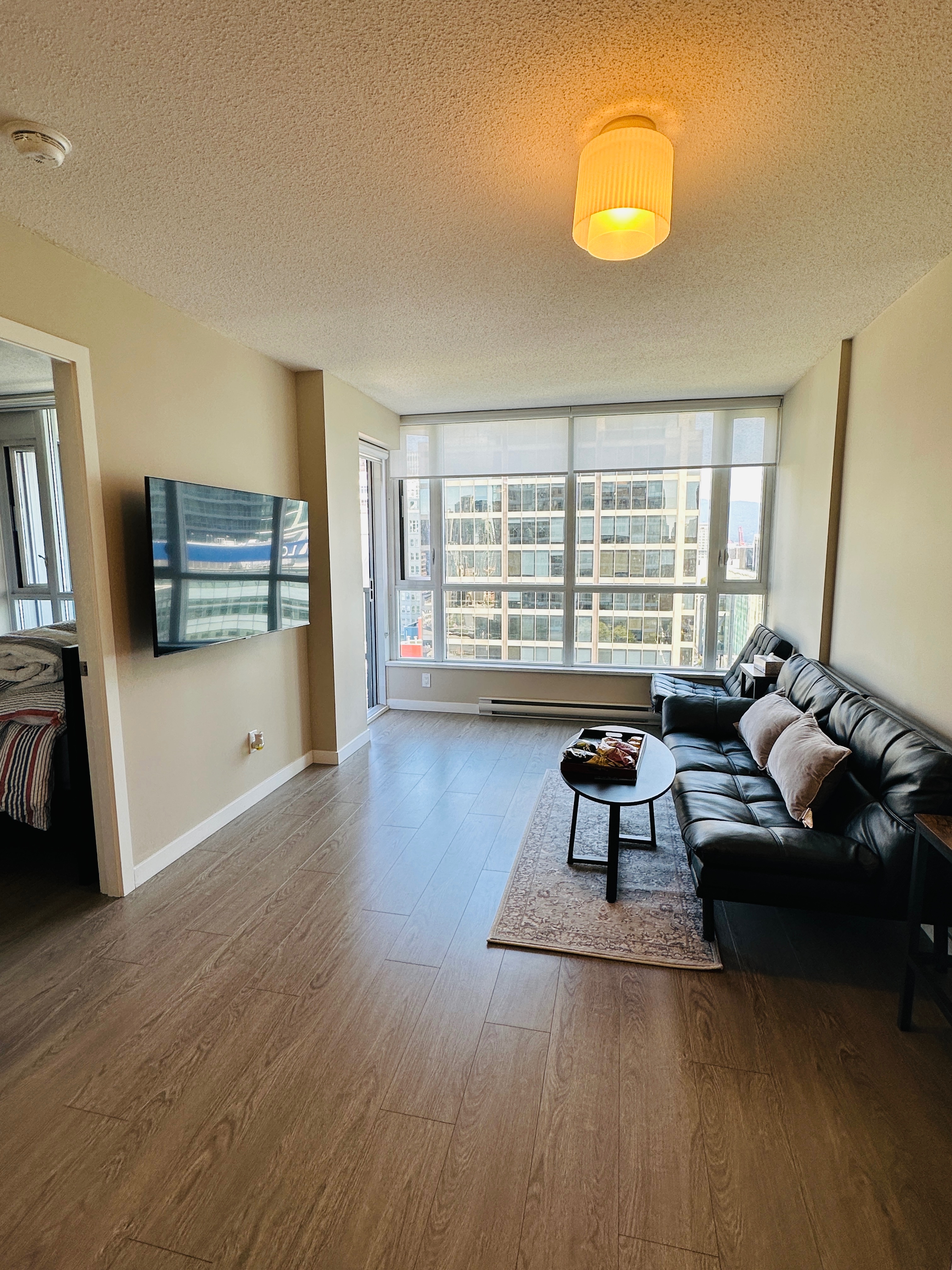 "Bright and modern living area with a large Smart TV, brand new flooring, and floor-to-ceiling windows offering great natural light."