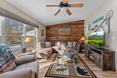 Bright, rustic lounge with sectional, big TV, and electric fireplace glow.