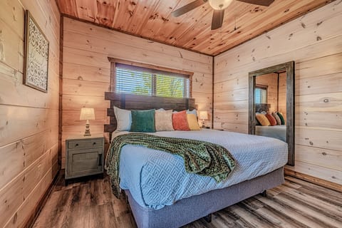 Cozy king bedroom with rustic wood walls, fan, and full-length mirror.