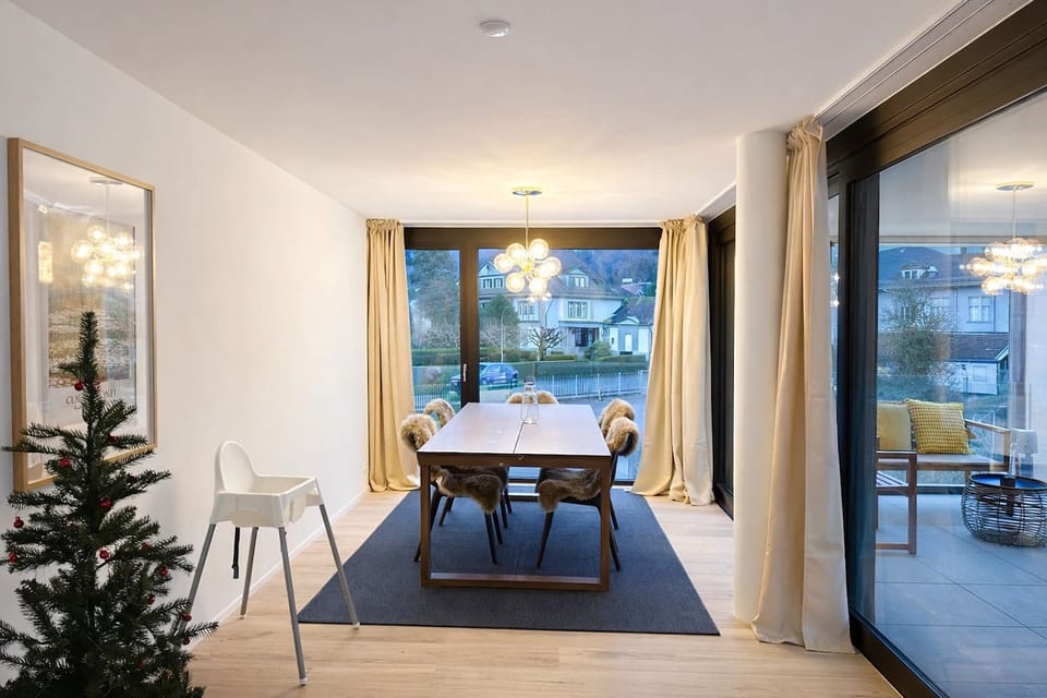 A bright open living and dining area with floor-to-ceiling windows, a large dining table, and direct access to the balcony.