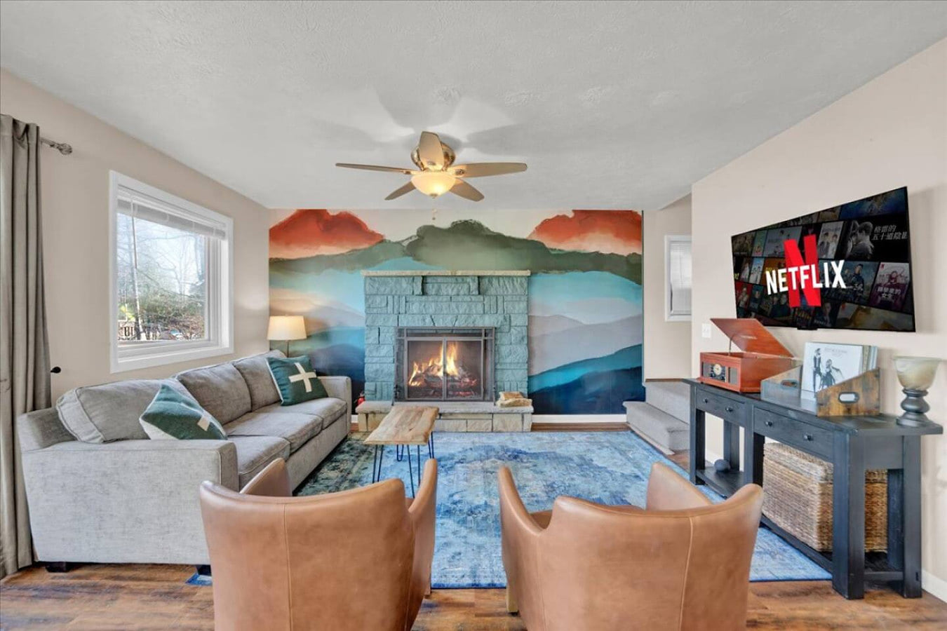 A bright and inviting living room with a cozy fireplace, TV, ceiling fan, and plenty of natural light pouring in through the windows—perfect for unwinding and enjoying the space.