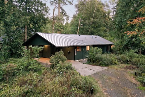 A classic green cabin tucked into the woods, glowing warm as evening settles in.