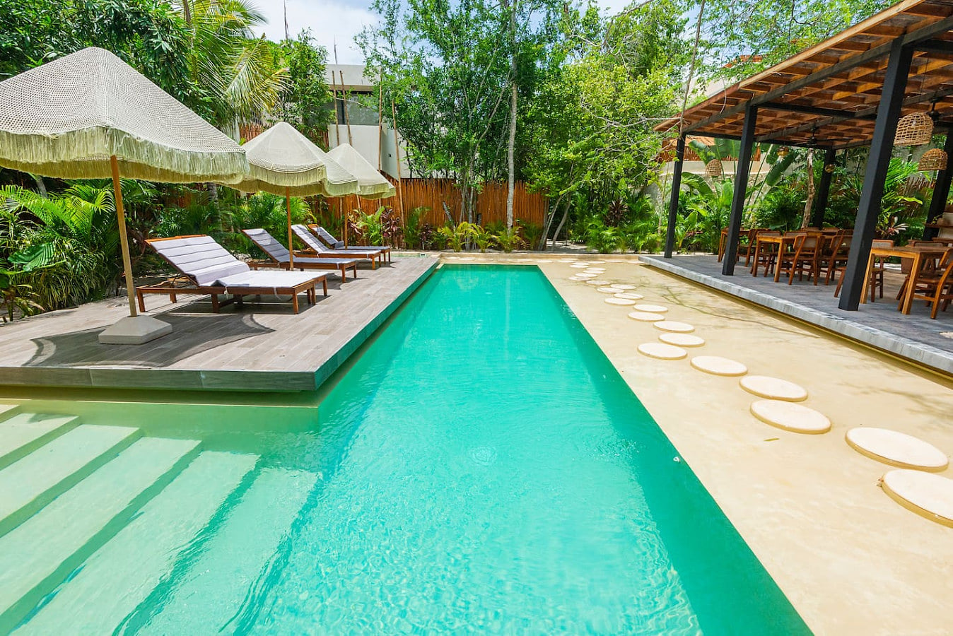 Tropical poolside escape. Enjoy a stunning swimming pool surrounded by lush greenery, comfy lounge chairs, and shaded areas—perfect for relaxation.