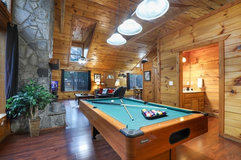 Rustic cabin lounge with pool table, stone fireplace, arcade, and vaulted ceilings