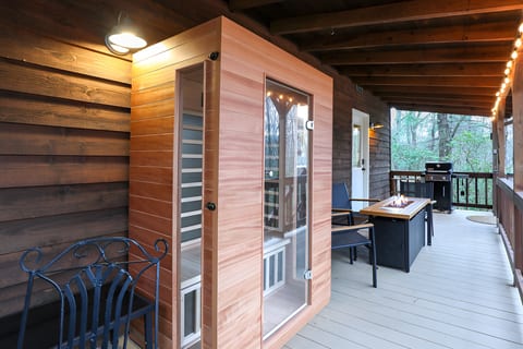 Covered deck with cedar sauna, fire table, grill, and forest views.