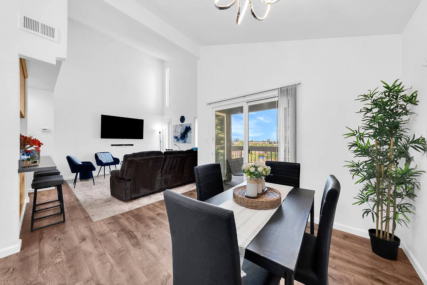 Bright dining area with seating for four, opening into the spacious living room and private balcony with tree-lined views.