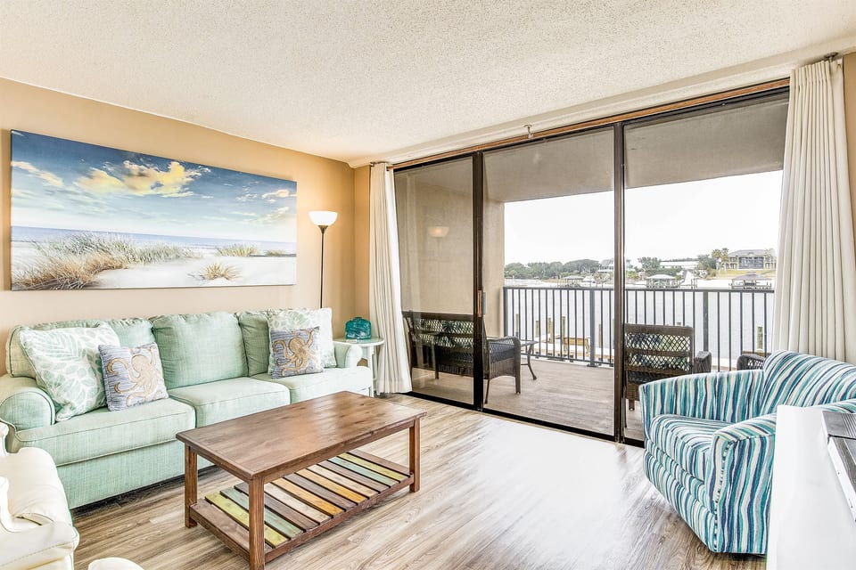 Coastal-inspired living area with flat-screen TV and sliding glass doors to covered balcony overlooking Old River Orange Beach