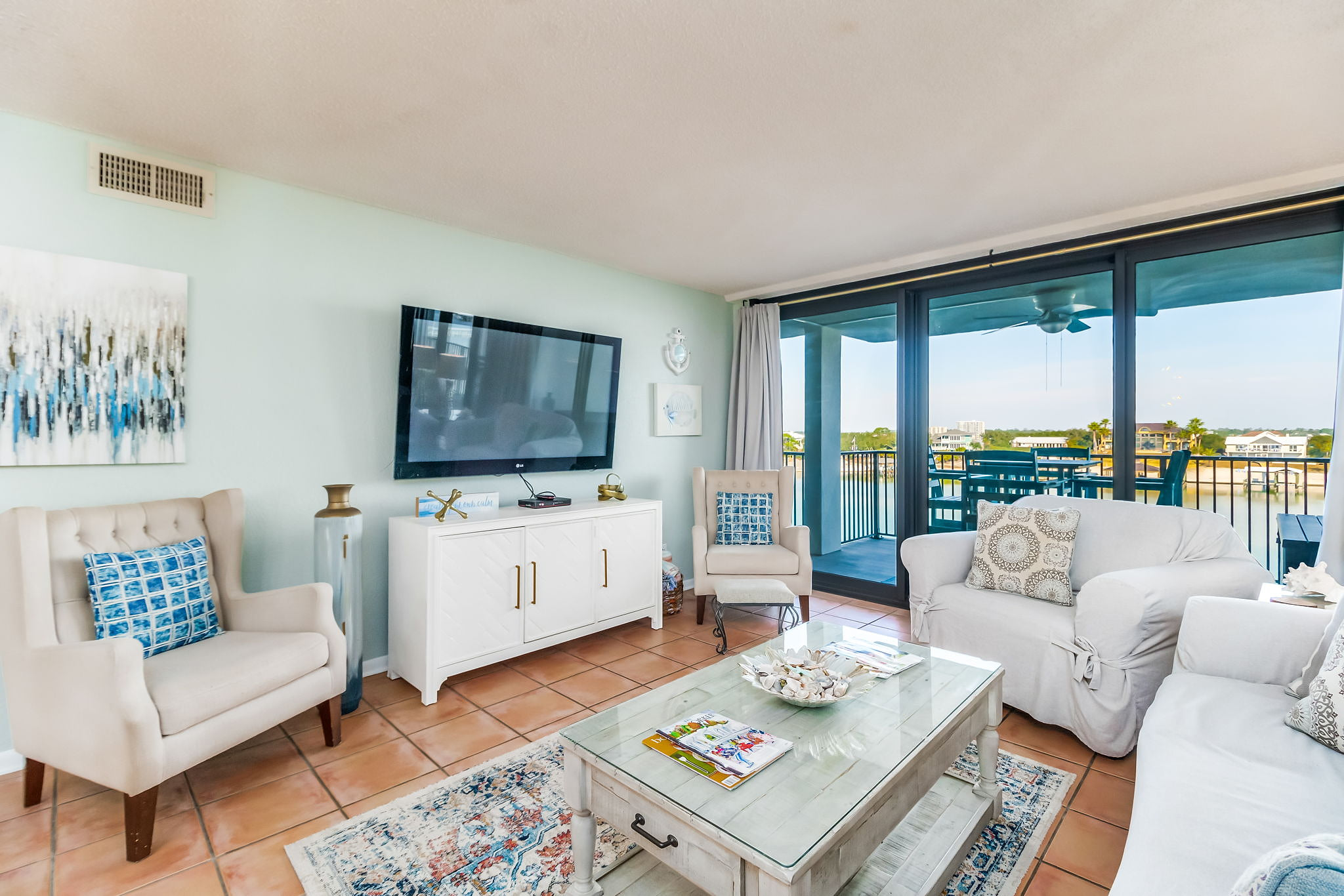 Coastal-inspired living area with flat-screen TV and sliding glass doors to covered balcony overlooking Old River Orange Beach