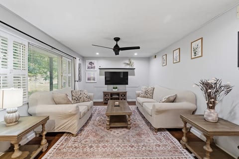 Bright, cozy living room with large windows, TV, and comfy seating