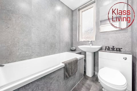 Modern full bathroom at Klass Living Short Lets & Serviced Accommodation Airdrie, featuring a bathtub with overhead shower, fresh towels, and essential amenities – a perfect space to relax and unwind.