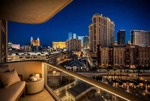 Private City-View Balcony — A furnished terrace with plush seating, intimate lighting, and sweeping views of the illuminated skyline and resort grounds.