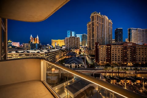 Private City-View Balcony — A furnished terrace with plush seating, intimate lighting, and sweeping views of the illuminated skyline and resort grounds.
