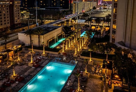 Illuminated Pool Terrace — A glowing outdoor pool surrounded by palm-lined decks, inviting loungers, and vibrant city lights creates a striking evening retreat.