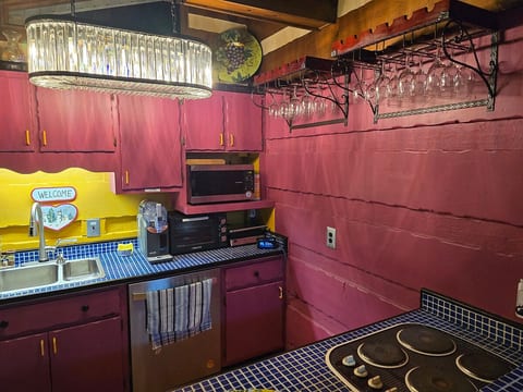 A closer look at the kitchen's eclectic charm, featuring a glamorous crystal chandelier and a convenient overhead wine glass rack. The bold fuchsia walls and yellow accents create a one-of-a-kind space for enjoying a glass of wine.
