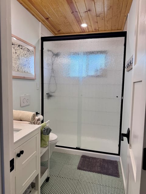 The remodeled bathroom features a walk in shower with textured glass, a wall mounted Toto toilet, and a ceiling heater and fan for year round comfort. Shampoo, conditioner, and body wash are provided.