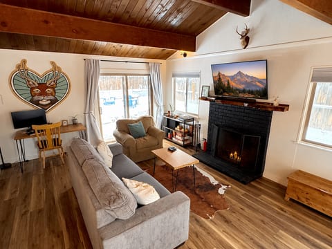 Warm, inviting living room with high wood beamed ceilings, fireplace, smart TV, and comfortable seating. Enjoy games, books, or music by the fire, or step through sliding doors to the fenced backyard. Includes a desk and monitor for remote work.