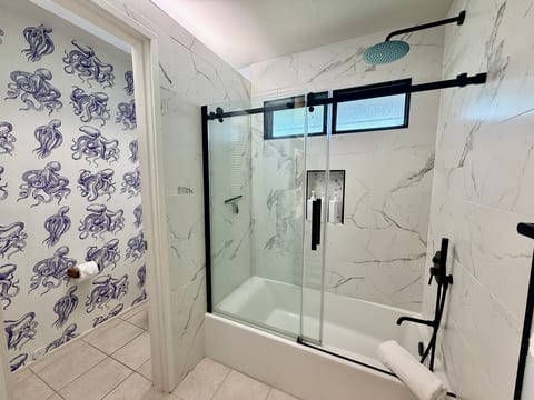 Modern spa-style bathroom with glass shower and playful coastal wallpaper