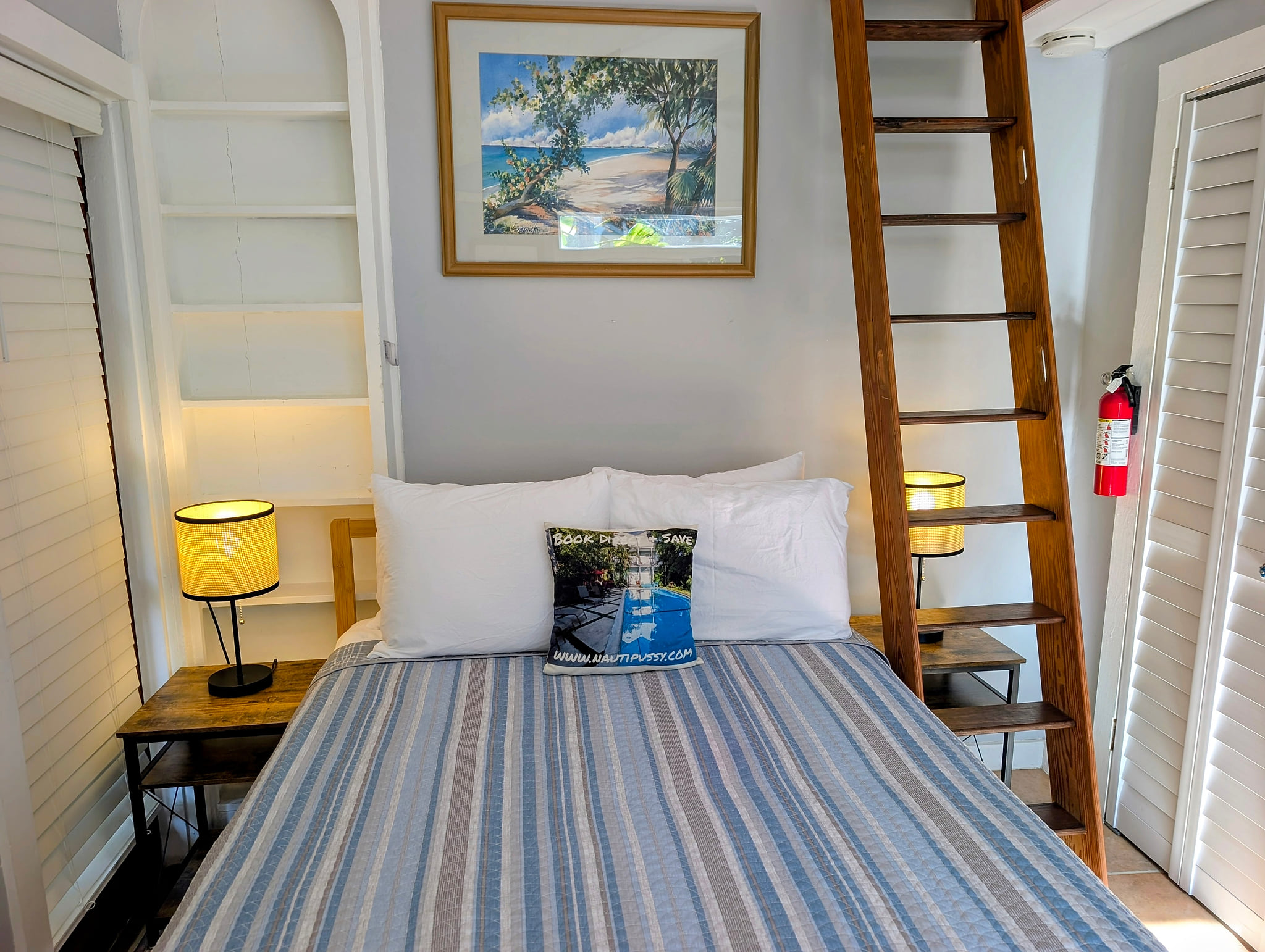 Cozy coastal nook with queen bed, warm lamps, and loft ladder