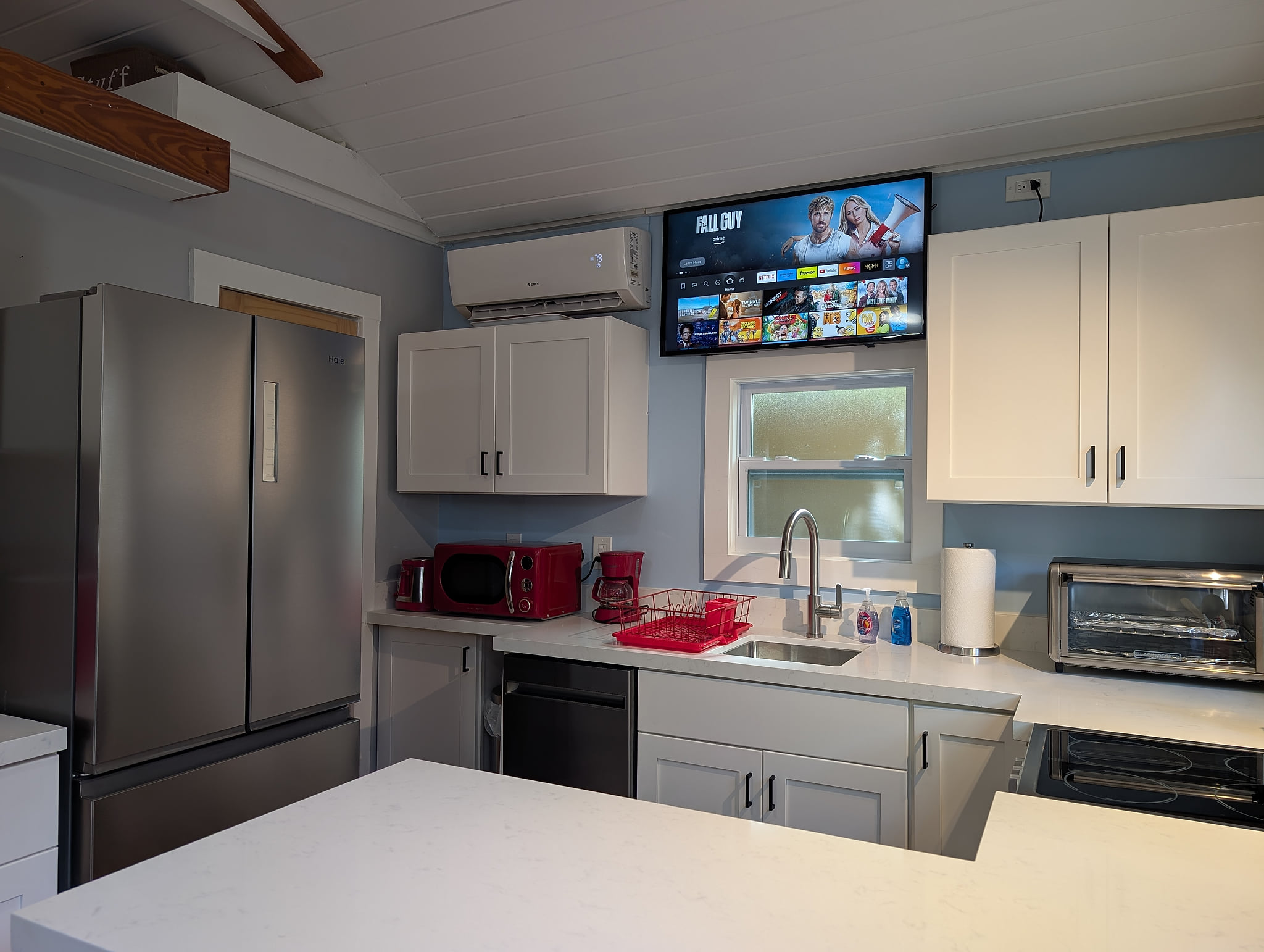 Modern kitchen with quartz island, smart TV, stainless fridge, and AC.