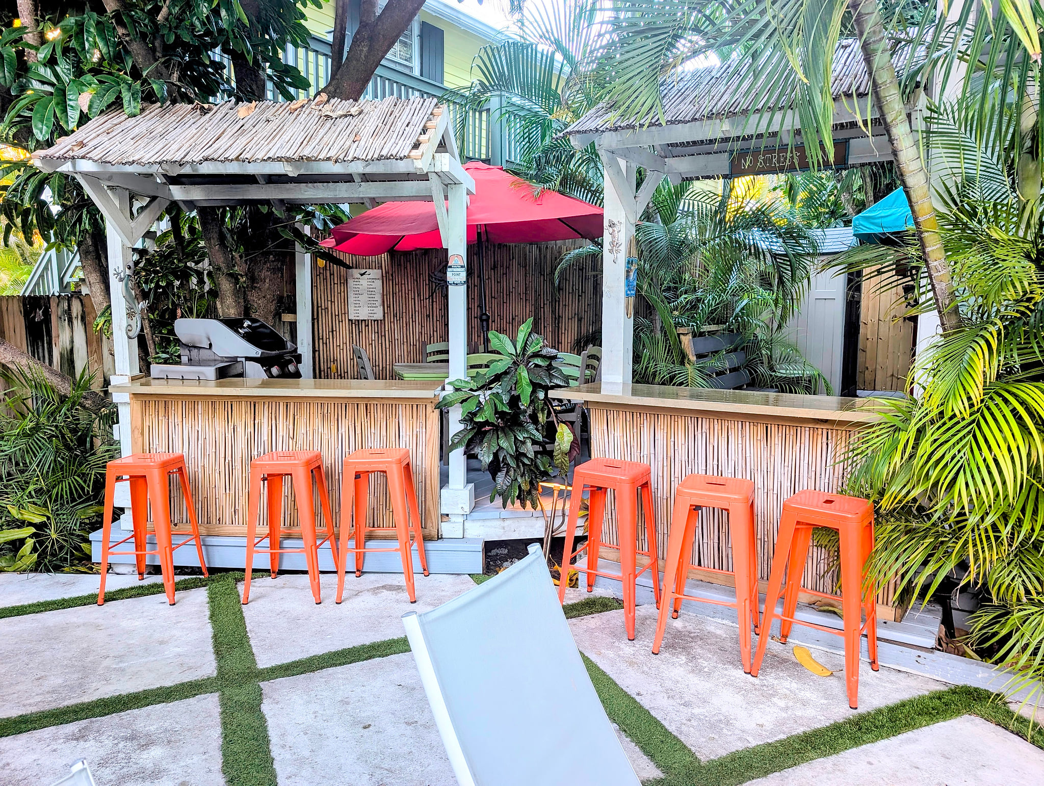 Tropical tiki bar patio with grill, bamboo counters, and bright stools