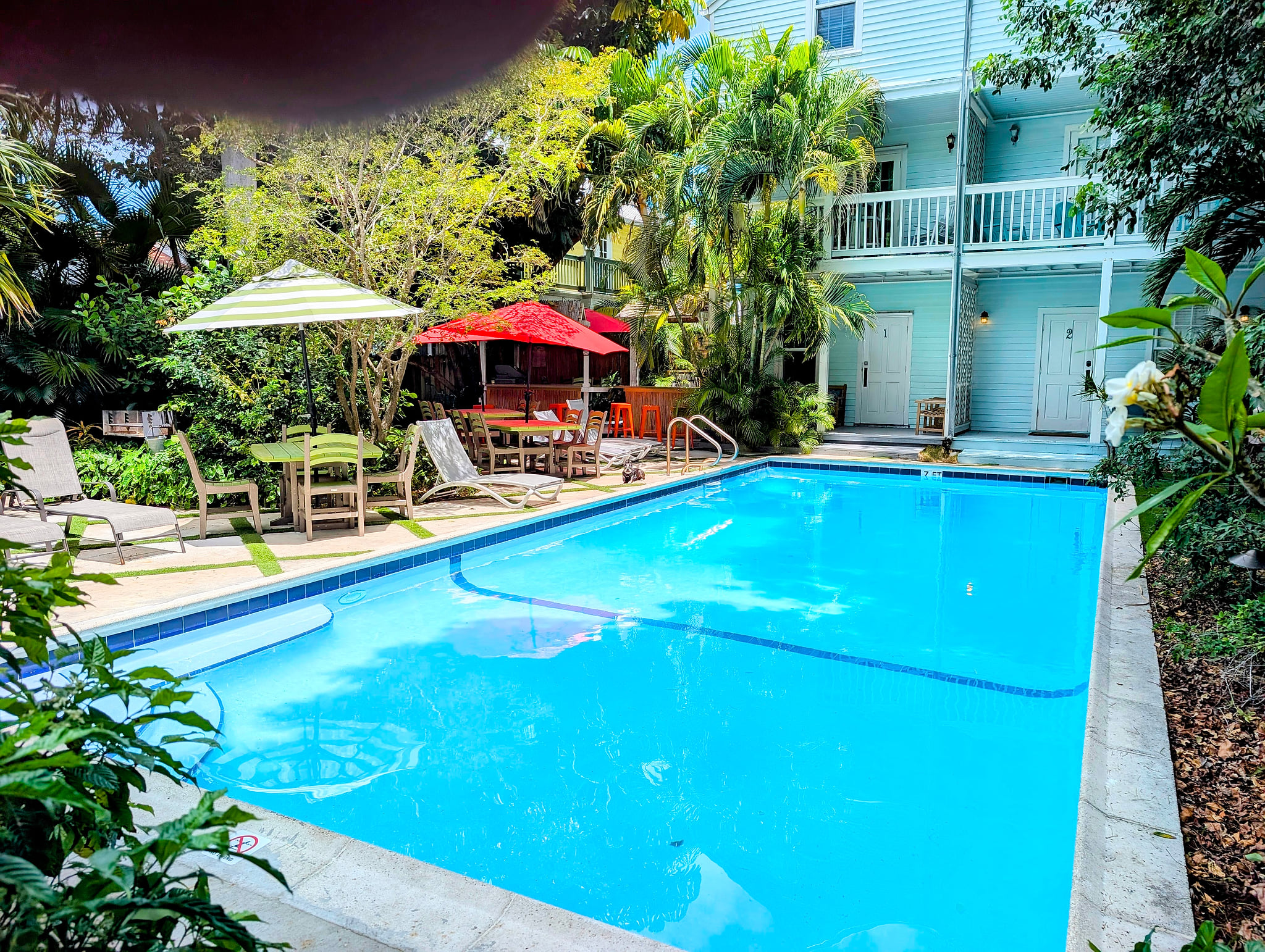 Tropical pool oasis with loungers, shaded seating, and balconies.